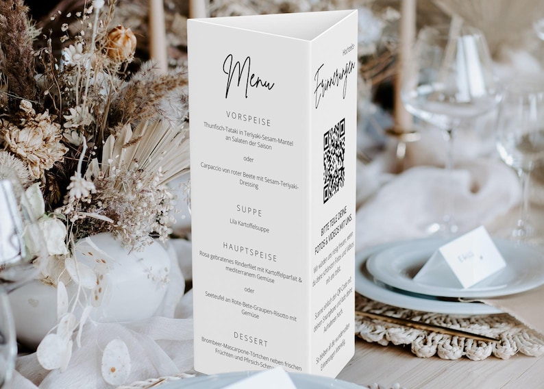 May include: A white, triangular menu card with black script, featuring sections for starters, soup, main course, and dessert. A QR code is printed on the side. The menu is set on a table with floral arrangements.