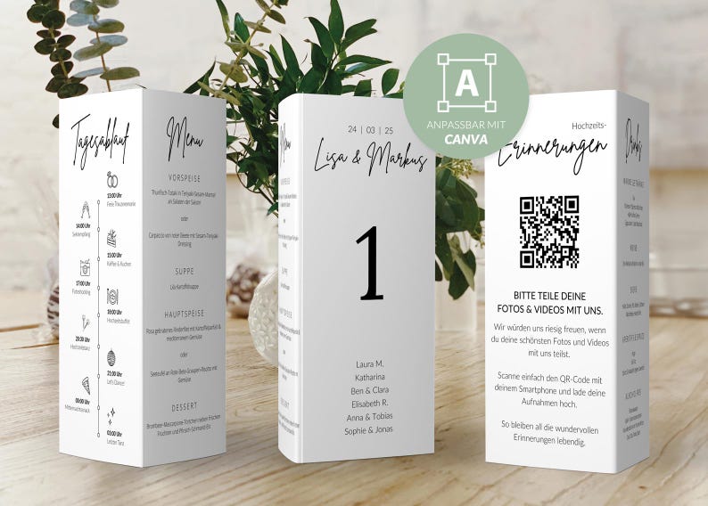 May include: White table cards with black text, displaying wedding information. One card shows a schedule, another a menu, and the third a table number and QR code. The cards are rectangular and stand on a wooden surface.