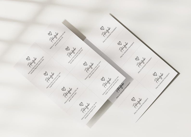 May include: Two white rectangular sheets featuring a grid of small cards with black text and a heart icon. Each card displays the German word Fotoaufgabe followed by specific instructions for guests to take photos, with some cards left blank for custom tasks.