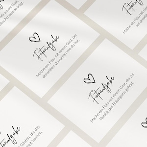 May include: A collection of white rectangular cards featuring the black text 'Fotoaufgabe' and a hand-drawn heart icon. Each card displays a unique German instruction for wedding guests to take specific photos, arranged in a repeating grid pattern.