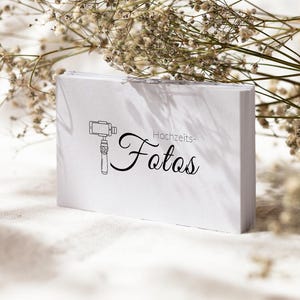 May include: A stack of white rectangular business cards featuring a black line drawing of a smartphone gimbal stabiliser and the text "Hochzeits-Fotos" in a combination of sans-serif and cursive black typography printed on the front surface.