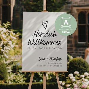 May include: A white sign on a wooden easel with the words "Herzlich Willkommen" and "Lisa + Markus" in black script. A heart symbol is above the text. The sign also includes the date "24. März 2026".