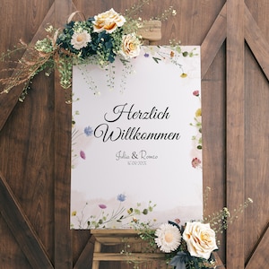 Könnte beinhalten: Ein weißes Hochzeitsschild mit floralen Akzenten und dem Text "Herzlich Willkommen Julia & Romeo 12.09.2025" auf einem Holzstaffelei.