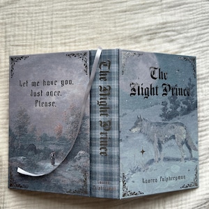 Puede incluir: Libro abierto titulado "The Night Prince" con una ilustración de un lobo en la portada. La portada es de color azul apagado con detalles florales decorativos. El lomo del libro tiene el texto "The Night Prince".
