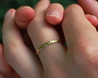 May include: Two hands clasped together, one hand wearing a thin gold band ring.