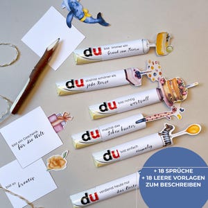 Peut inclure: Plusieurs barres chocolat&eacute;es d&eacute;cor&eacute;es avec du texte allemand, avec des phrases comme &laquo; Tu es un cadeau pour le monde &raquo; et &laquo; Tu m&eacute;rites le meilleur aujourd'hui &raquo;. Des d&eacute;coupes d&eacute;coratives incluent une baleine, un crayon et des bo&icirc;tes cadeaux.