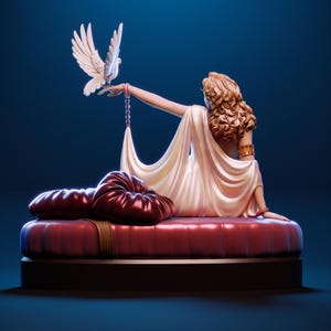 Puede incluir: Una escultura de una mujer con un vestido blanco fluido, sentada sobre un coj&iacute;n rojo, con una paloma blanca posada en su mano. La mujer tiene el pelo rubio rizado y lleva pulseras doradas. La escultura est&aacute; sobre un fondo azul oscuro.
