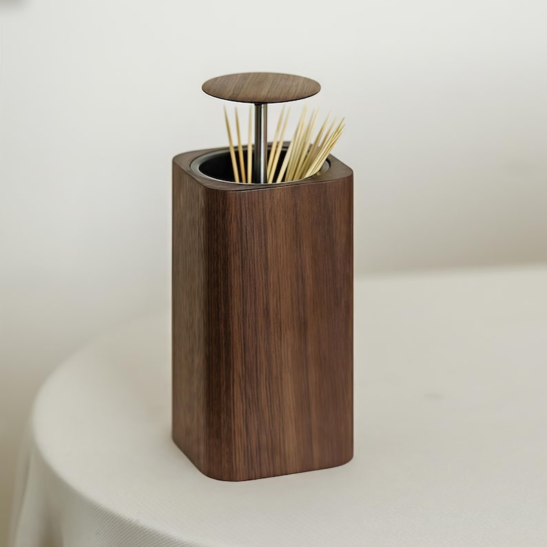 May include: A wooden toothpick holder with a square base and a circular top. The holder is made of dark brown wood and contains a bundle of toothpicks. The top is attached to the base by a metal rod.