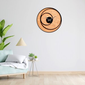 May include: A modern wall clock with a black circular frame and wooden background. The clock face is black with silver hands and a concentric circle design.