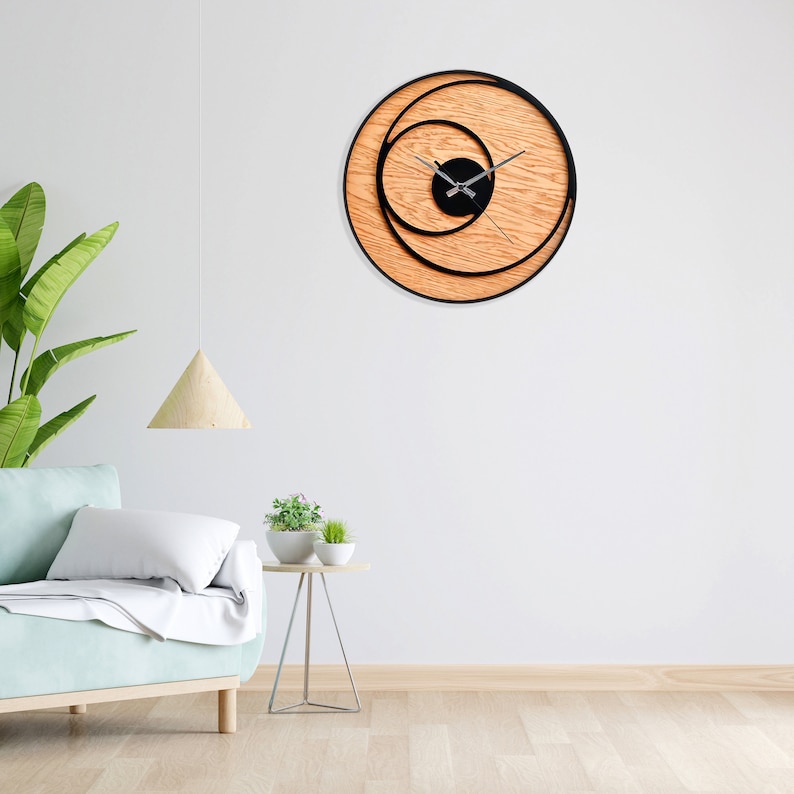 May include: A modern wall clock with a black circular frame and wooden background. The clock face is black with silver hands and a concentric circle design.