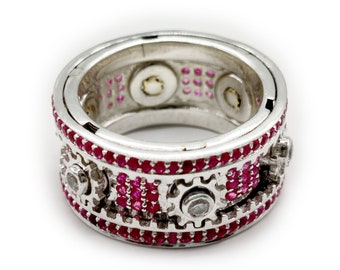 May include: A silver ring with a spinning gear design. The ring is decorated with small red gemstones and clear stones.