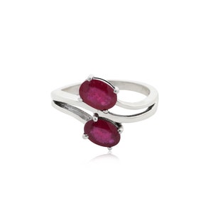 May include: A silver ring featuring two oval-cut, deep red gemstones. The gemstones are set in a split-shank design, creating a modern and elegant look. The ring is displayed against a white background.