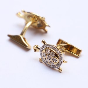 May include: Gold-toned cufflinks in the shape of turtles. The turtle's shell is encrusted with small, clear gemstones. The cufflinks have a classic post and toggle closure.