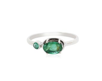 May include: A silver ring with two oval-shaped emerald gemstones. The larger emerald is set in a prong setting and the smaller emerald is set in a bezel setting.