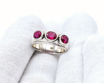 May include: A silver ring with three oval-shaped ruby red gemstones set in a textured band.