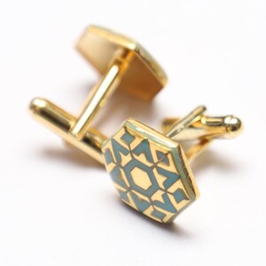 May include: A pair of gold cufflinks with a geometric design. The cufflinks have a blue and gold enamel pattern.
