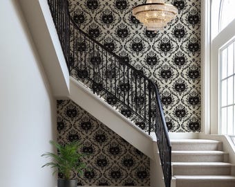 May include: A staircase with black wrought iron railings and a patterned wallpaper featuring black cat faces on a cream background. A crystal chandelier hangs above the stairs. A potted plant and a patterned rug are at the base of the stairs.