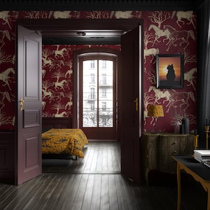 May include: A bedroom with dark wood flooring and burgundy walls decorated with a gold horse pattern. The room features an open doorway, a bed with a yellow patterned blanket, and a framed picture of a cat.