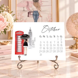 Pode incluir: Uma p&aacute;gina de calend&aacute;rio de mesa branca para outubro com uma ilustra&ccedil;&atilde;o a preto e branco de uma pessoa com um guarda-chuva preto ao lado de uma cabine telef&oacute;nica vermelha e do Big Ben. A grelha mostra os dias do m&ecirc;s em preto.