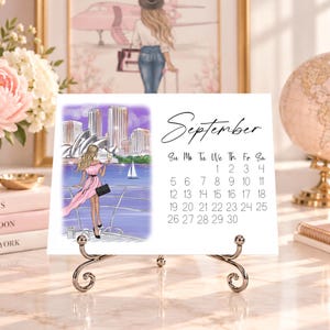 Pode incluir: Um calend&aacute;rio de mesa para setembro num suporte de metal prateado. O lado esquerdo apresenta uma ilustra&ccedil;&atilde;o de uma pessoa com um vestido cor-de-rosa com vista para o horizonte da cidade e um porto. O lado direito mostra o m&ecirc;s e as datas.