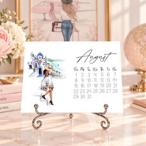Pode incluir: Uma p&aacute;gina de calend&aacute;rio de mesa branca para agosto com um cabe&ccedil;alho em letra cursiva preta e uma grade de datas. O lado esquerdo exibe uma ilustra&ccedil;&atilde;o em aquarela de uma pessoa de vestido branco descendo escadas em dire&ccedil;&atilde;o a uma vila costeira.