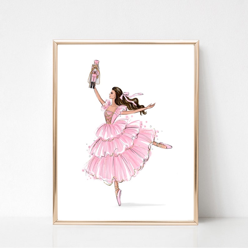 May include: A ballerina in a pink tutu holds a nutcracker doll in her right hand. She is wearing pink ballet shoes and has her left leg extended in a dance pose.