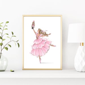 May include: A framed illustration of a ballerina in a pink tutu holding a nutcracker doll. The ballerina is wearing pink ballet shoes and has blonde hair. The background is white.