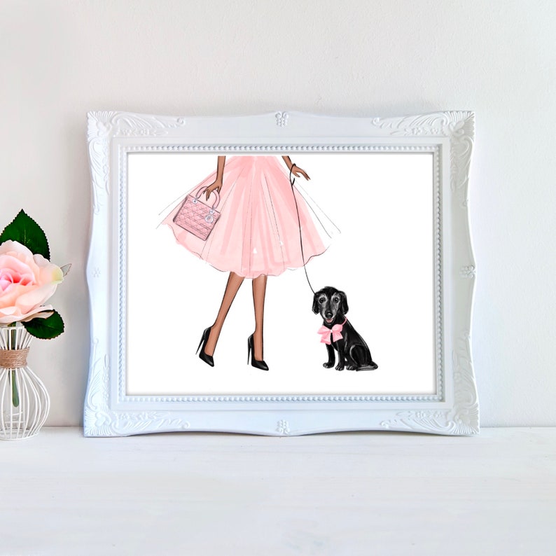 Op de afbeelding: Een vrouw in een roze jurk loopt met een zwarte hond met een roze strik op een witte achtergrond.