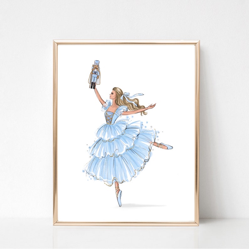 May include: A ballerina in a blue and gold tutu holds a nutcracker doll in her right hand. She is dancing on pointe with her left leg extended. The background is white.