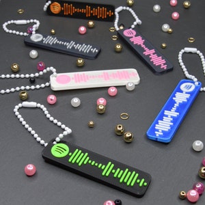 Könnte beinhalten: Ein Set aus sieben bunten Schlüsselanhängern mit Barcode-Design. Die Schlüsselanhänger sind aus Kunststoff und haben verschiedene Farben, darunter Blau, Grün, Pink, Weiß und Schwarz. Die Schlüsselanhänger hängen an einer weißen Oberfläche.