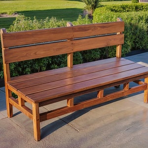 Może przedstawiać: Drewniana ławka z oparciem i siedziskiem z listew. Ławka wykonana jest z ciemnobrązowego drewna i ma prosty, rustykalny design.