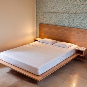 May include: A wooden platform bed frame with a white mattress and two white pillows. The headboard is made of wood and has a light wood finish. There is a small bedside table on each side of the bed.