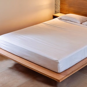 Puede incluir: Una cama blanca con un marco y cabecera de madera. La cama est&aacute; hecha con s&aacute;banas y almohadas blancas.