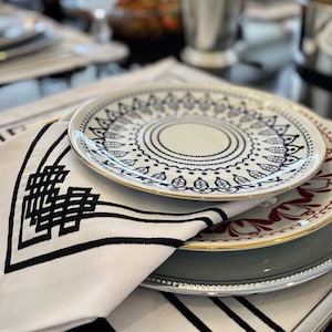 May include: A set of three white dinner plates with blue and gold trim. The top plate has a circular design with blue and white details. The middle plate has a red and gold floral design. The bottom plate is a light gray color with a silver rim.