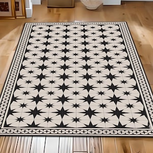 May include: Black and white geometric patterned rug with a border of repeating chain-like designs. The rug has a cream background with black star-shaped designs.