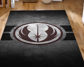 May include: A black and gray area rug with a distressed look features a white and gray Jedi Order symbol with a brown lightsaber and wings. The symbol is surrounded by a white circle and two gray stripes.