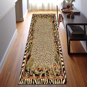 Könnte beinhalten: Ein rechteckiger Teppich mit einem Leopardenmuster in der Mitte, umrahmt von einem Rand aus Zebrastreifen und tropischen Blättern. Das Design des Teppichs verwendet Farbtöne von Beige, Braun, Schwarz und Grün und schafft einen auffälligen dekorativen Akzent.