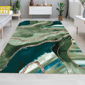 May include: Abstract area rug with a green, blue, and gold design. The rug features a wavy pattern with a metallic gold accent.