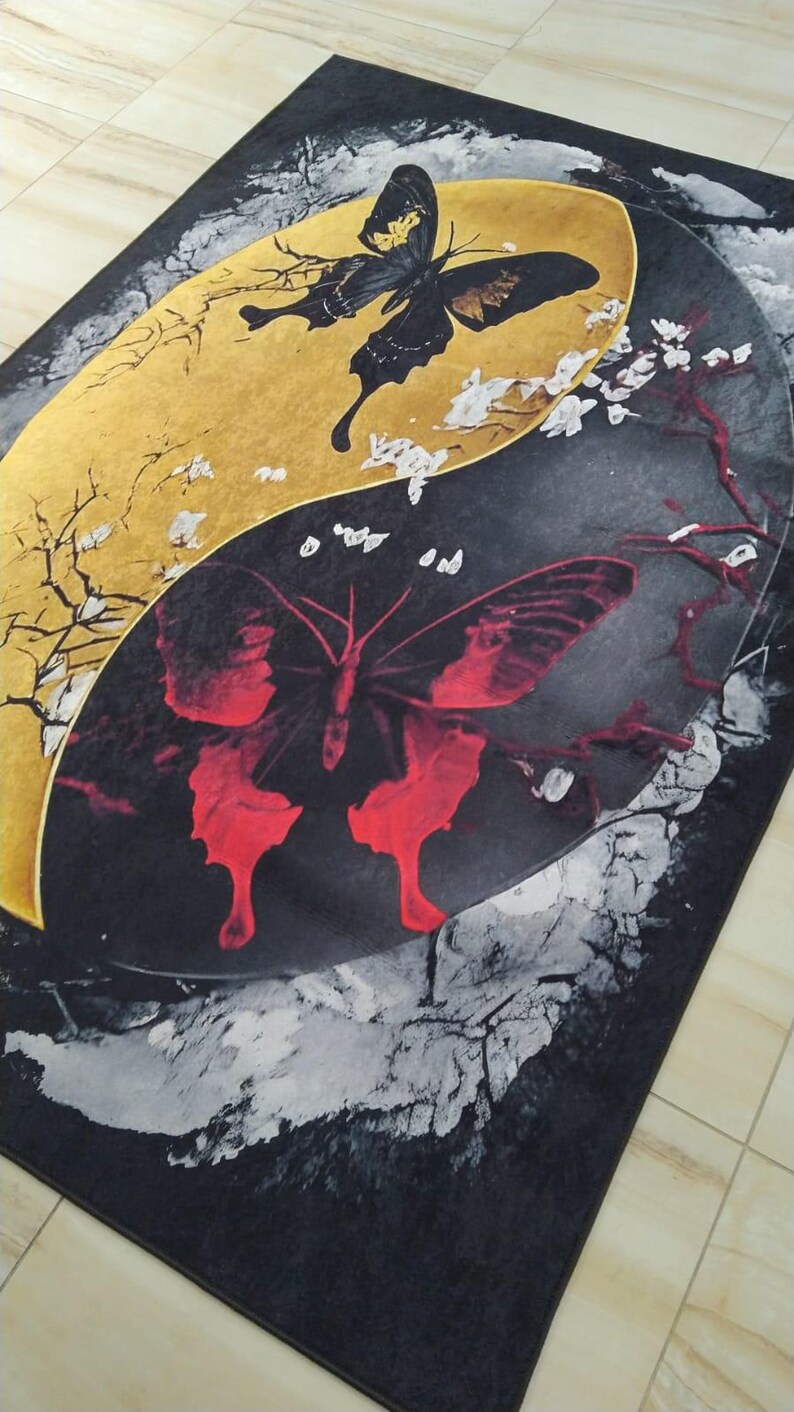 May include: A black and gold rug with a yin yang design featuring two butterflies. The butterfly on the gold side is black and the butterfly on the black side is red.