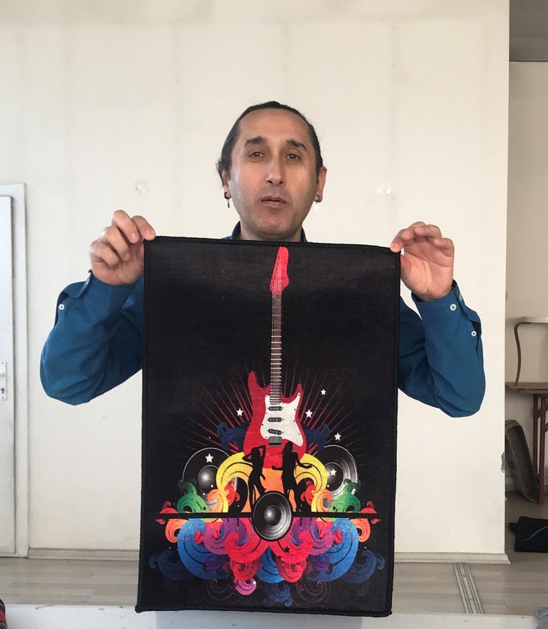 May include: A black and colorful guitar-themed mousepad with a red electric guitar, colorful swirls, and a speaker. The mousepad is being held by a person.