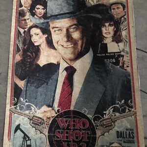 May include: A vintage poster with the text "WHO SHOT J.R.?" and images of people, guns, an oil rig, and a house. The central figure is a smiling man in a hat. The poster has a red border and a distressed look.