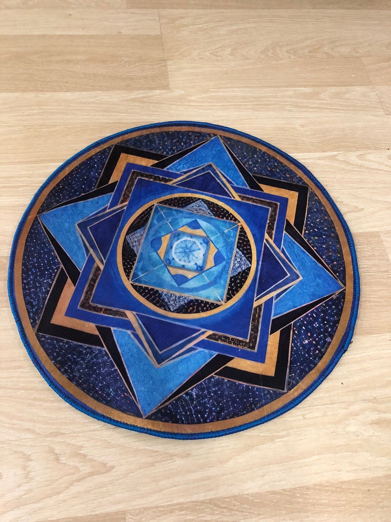 Op de afbeelding: Een rond blauw en gouden mandala-kleed met een geometrisch patroon. Het kleed heeft een blauwe rand en een gouden midden.