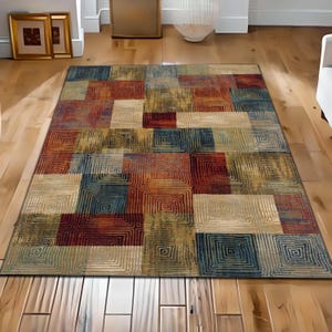 Può includere: Un tappeto rettangolare con un motivo geometrico. Il tappeto presenta quadrati nei toni del rosso, blu, beige e oro. Ogni quadrato ha un motivo quadrato concentrico. Il tappeto è posato su un pavimento in legno.