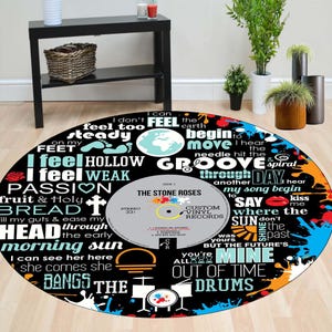 Könnte beinhalten: Runder schwarzer Teppich mit Vinyl-Schallplatten-Design. Der Teppich zeigt Songtexte und ein Etikett mit der Aufschrift "The Stone Roses". Bunte Farbspritzer und Grafiken von Musikinstrumenten verzieren den Rand. Der Teppich hat einen Durchmesser von ca. 152 cm.