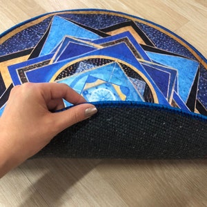 Op de afbeelding: Een rond blauw en gouden mandala-kleed met een zwarte rand. Het kleed is dubbelgevouwen, waardoor de donkerblauwe achterkant zichtbaar is.
