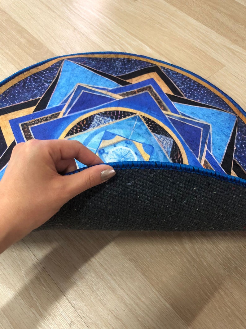 Op de afbeelding: Een rond blauw en gouden mandala-kleed met een zwarte rand. Het kleed is dubbelgevouwen, waardoor de donkerblauwe achterkant zichtbaar is.