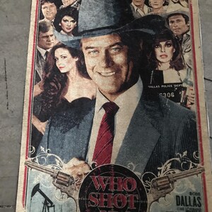 May include: A retro poster with a central image of a man in a hat, with other people around him. The poster includes the text "WHO SHOT JR?" in a circular design, with images of guns and oil derricks. The CBS Dallas logo is also visible.