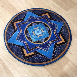 Op de afbeelding: Een rond blauw en gouden mandala-kleed met een geometrisch patroon. Het kleed heeft een blauwe rand en een gouden midden.