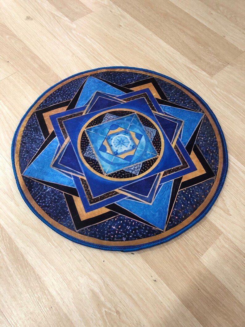 Op de afbeelding: Een rond blauw en gouden mandala-kleed met een geometrisch patroon. Het kleed heeft een blauwe rand en een gouden midden.
