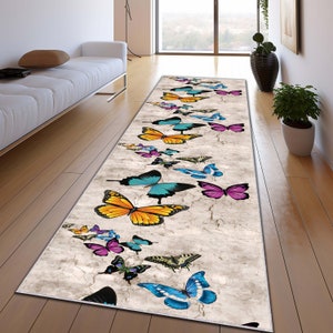 May include: A long runner rug with a white background and a pattern of colorful butterflies. The butterflies are in various shades of blue, yellow, pink, and purple.